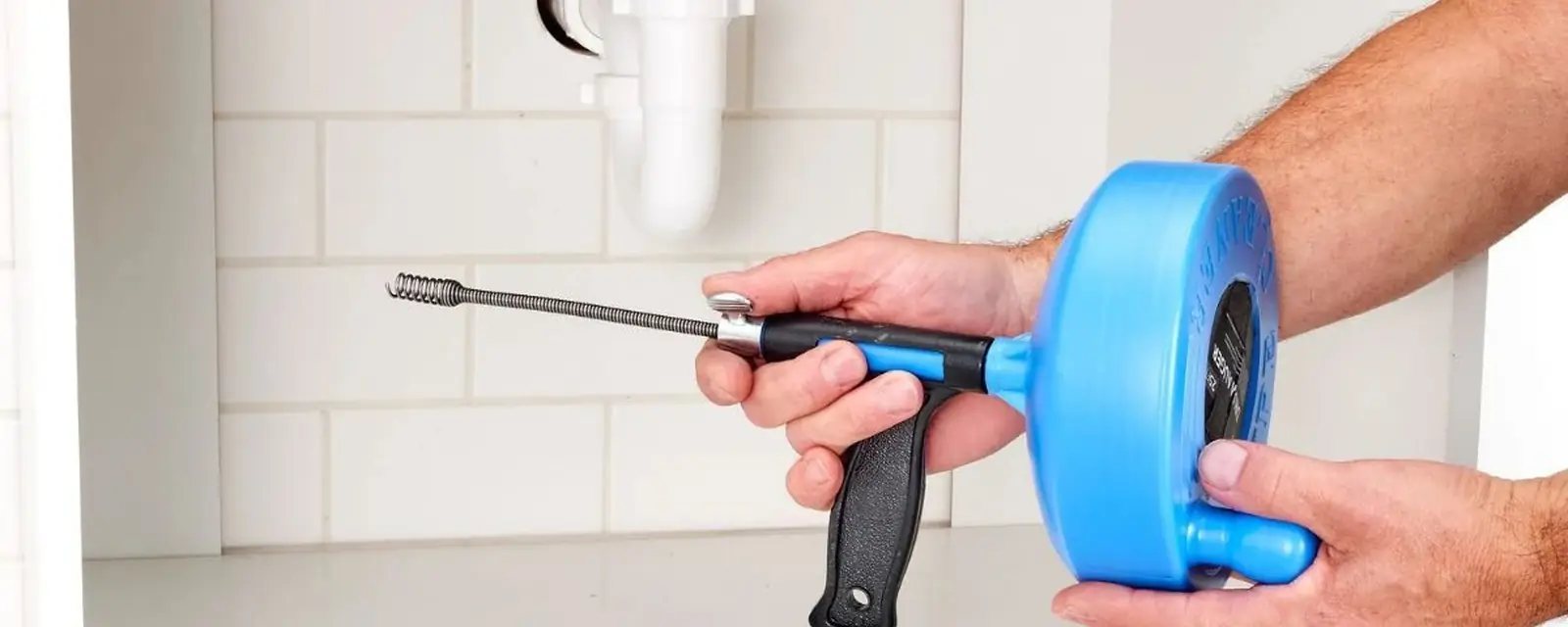Hand drain snake held under a sink beside the trap
