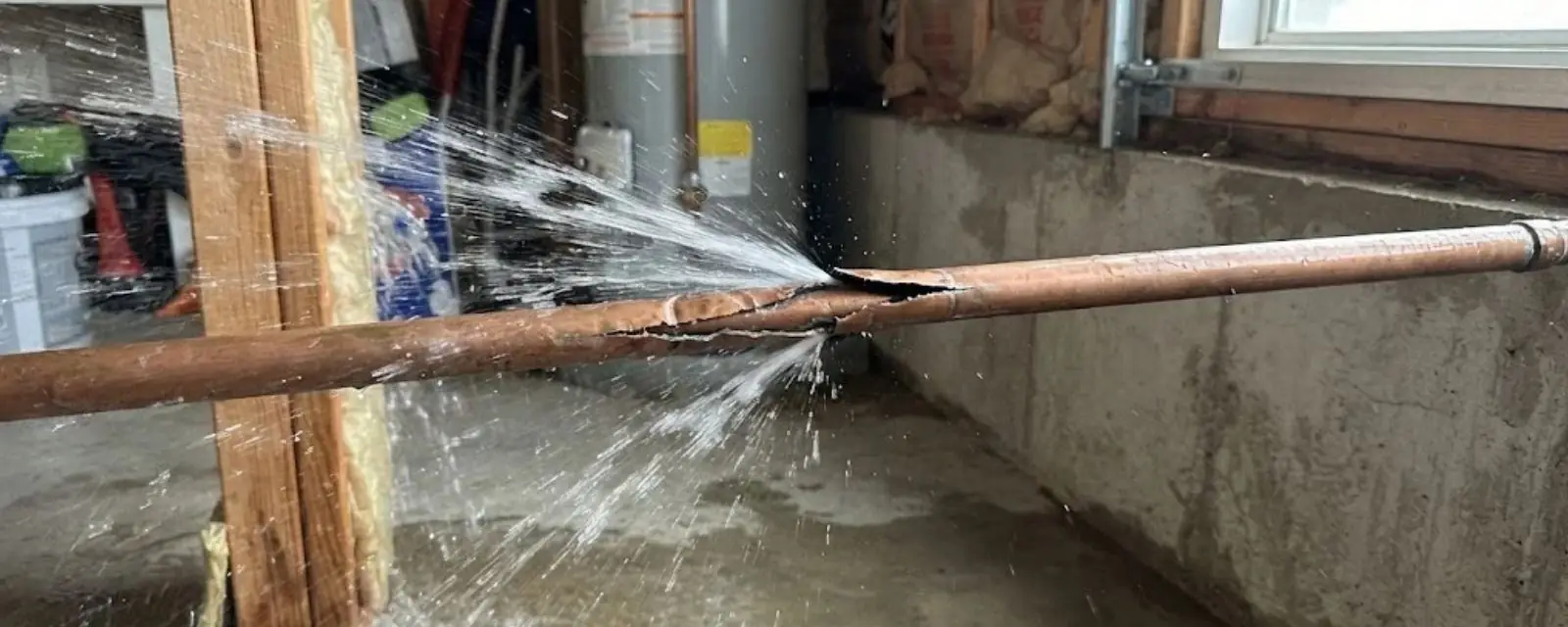 Water pipe split open and spraying water across a basement wall and floor